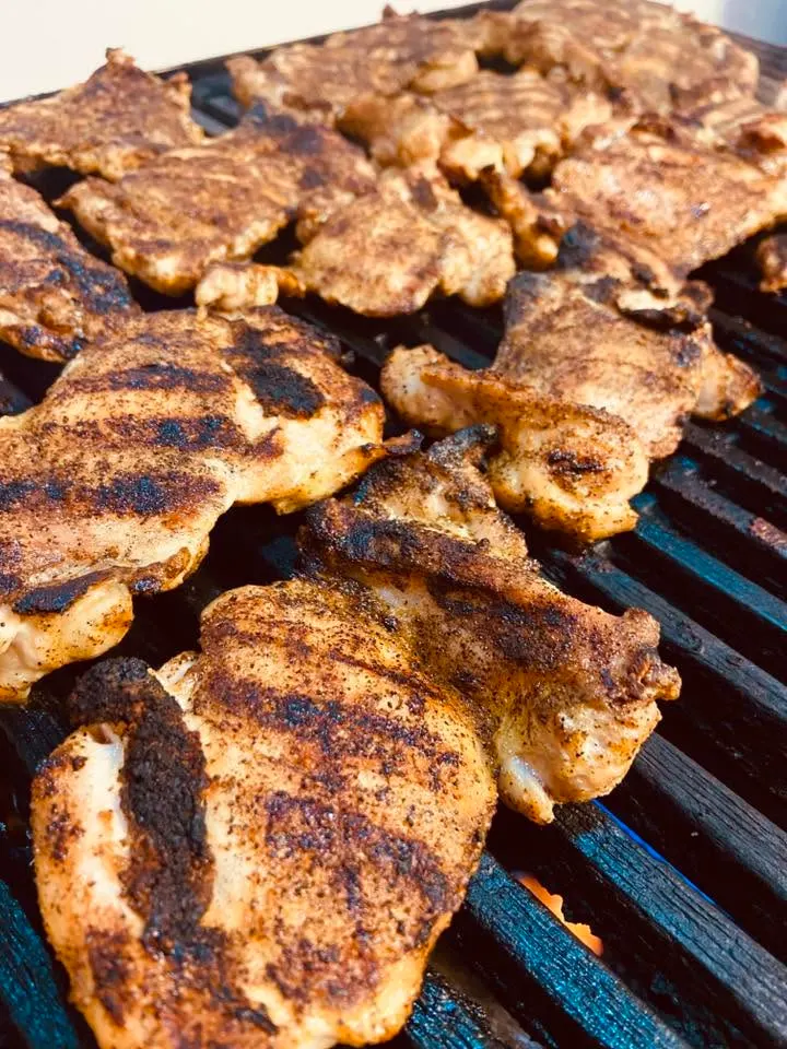 Seasoned chicken thighs char-grilling over an open flame