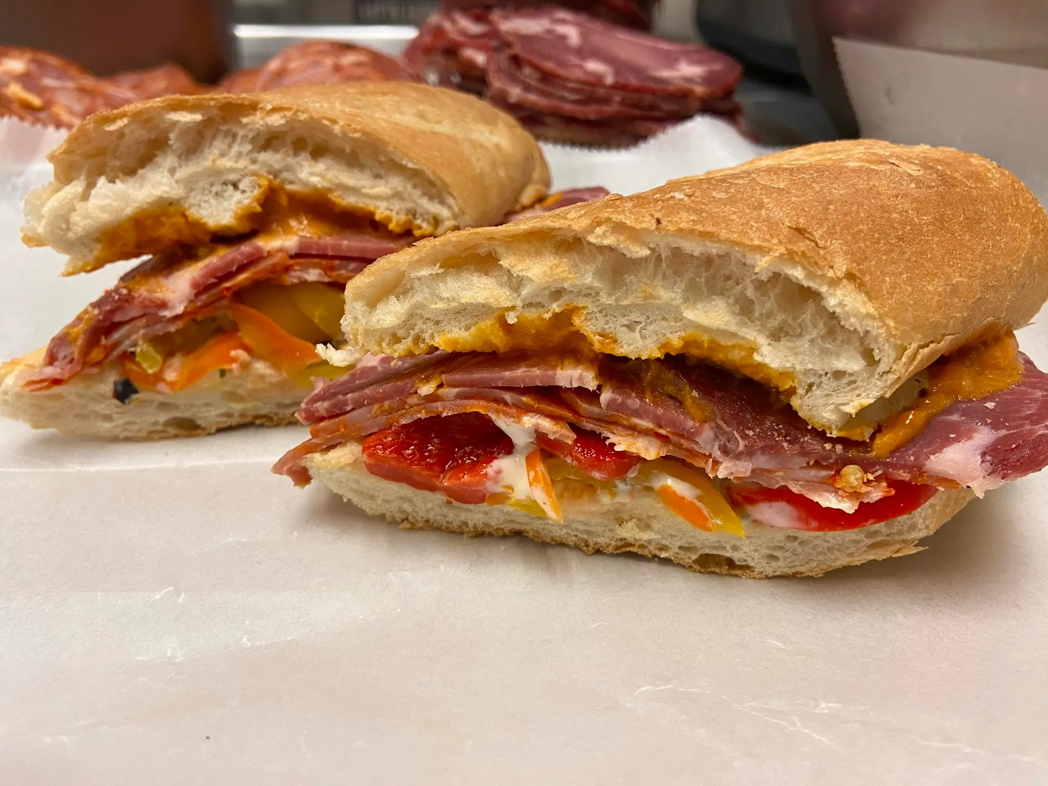A pressed Italian sub sliced in half, layered with cured meats, roasted peppers and banana peppers on a fresh baguette