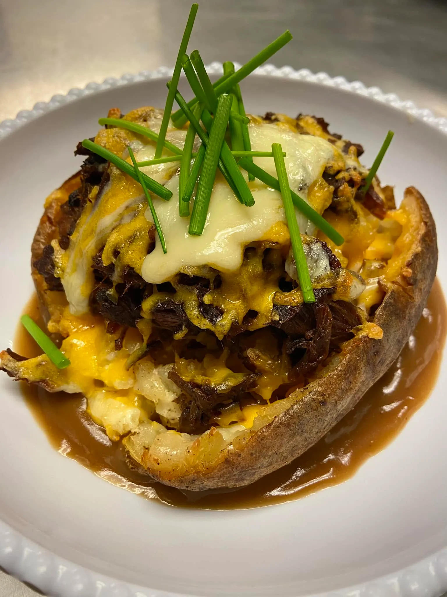 Twice baked loaded potato topped with braised beef, melted cheese, gravy and fresh chives